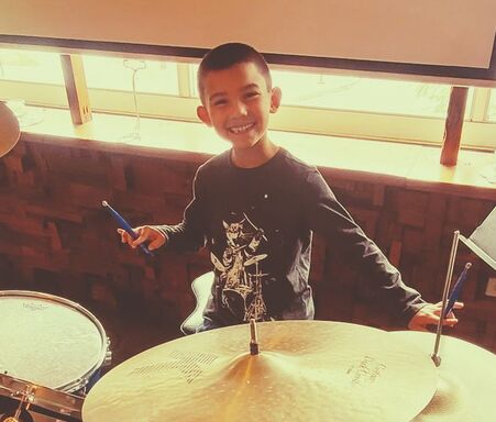 Picture of a kid smiling in front of the drums after a kids drum lesson. 