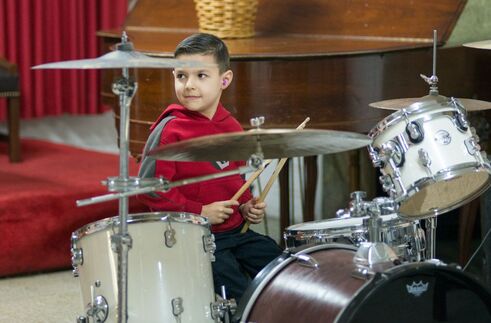 Picture of one of our 6 year old drum students sitting in front of our drum set at one of our drum day showcase days. We do a showcase for our students every 6 months
